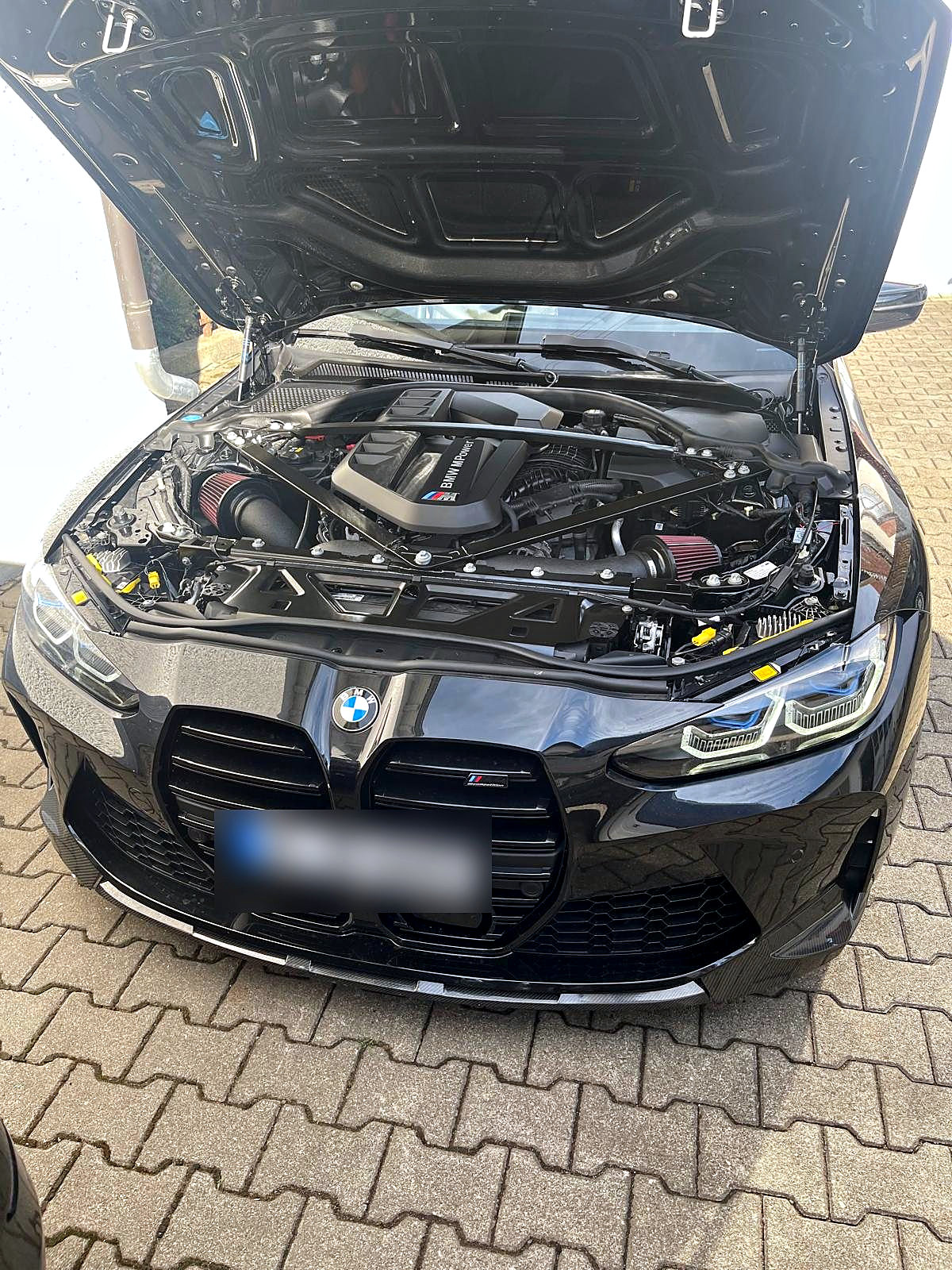 BMW M4 mit geöffneter Motorhaube vor der Halle, der Reihensechszylinder liegt frei