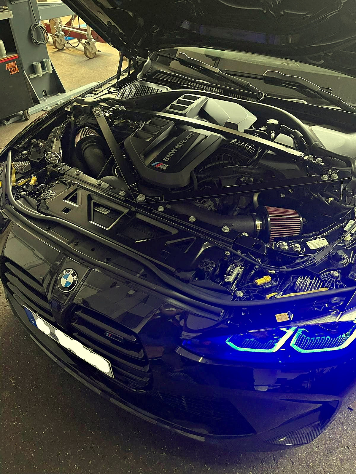 BMW M4 in der Halle mit offener Motorhaube und blau leuchtendem Tagfahrlicht