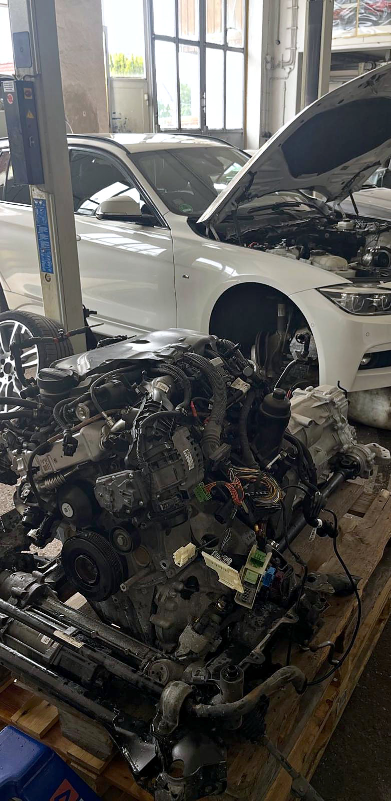 Blick in die Halle in Weil: BMW mit offener Haube, davor der ausgebaute Motor