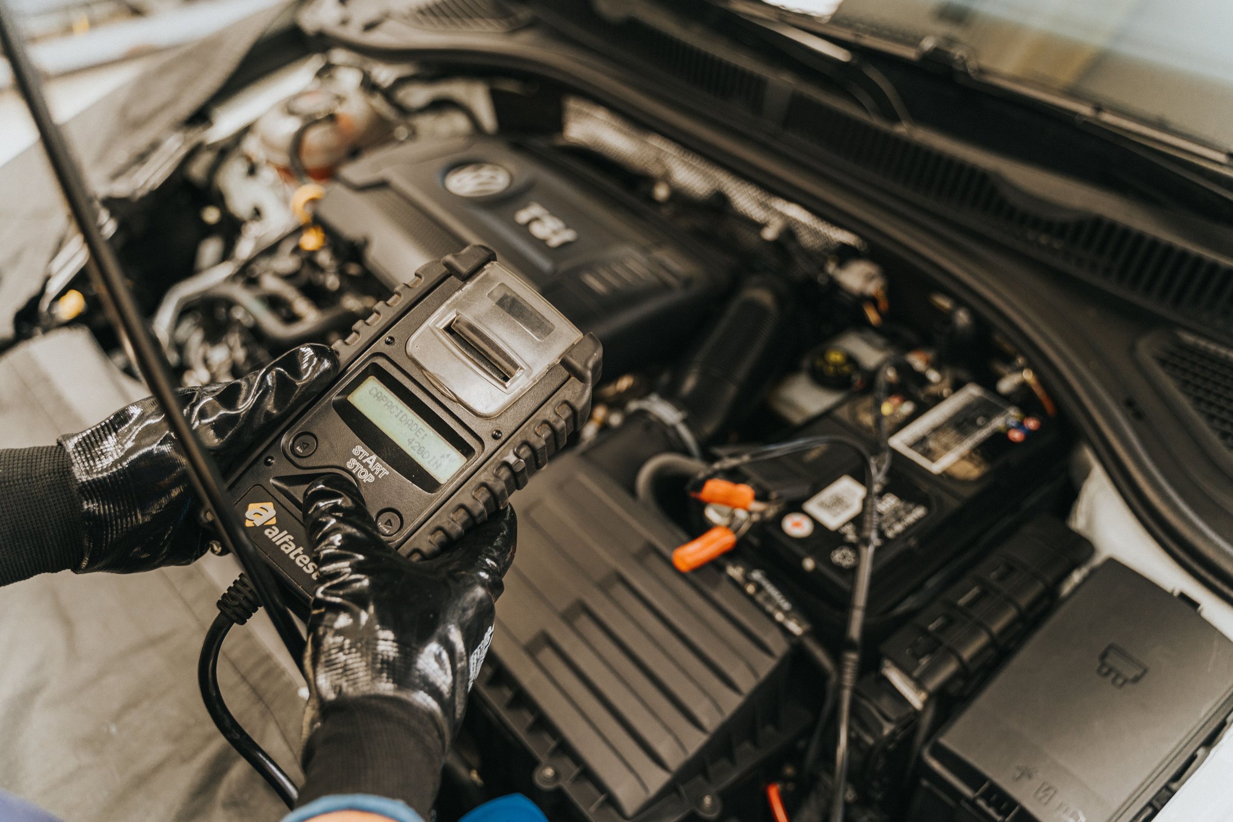 Batterie- und Bordnetztest: Prüfgerät in der Hand, angeschlossen an die Batterie im offenen Motorraum